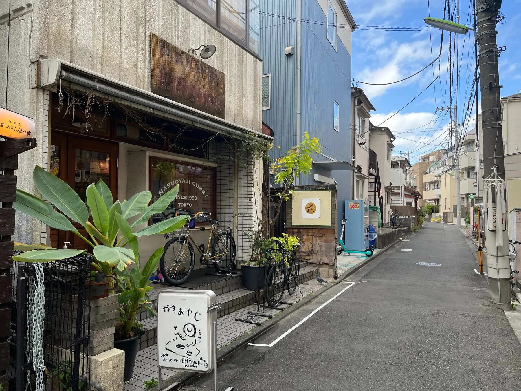 茄子おやじの建つ代沢の路地。空が広く、店先に鉢植えが並ぶ